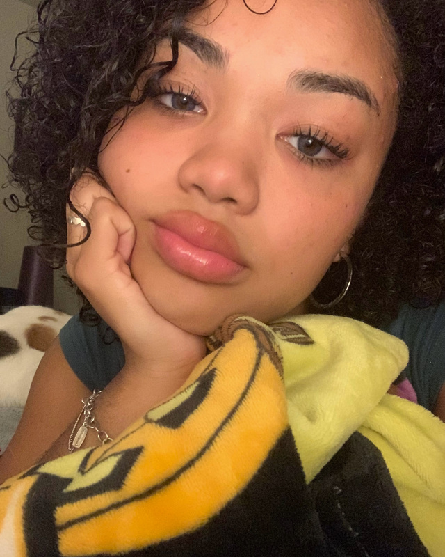 A young woman wearing a charm bracelet relaxes on a bed with a blanket.