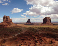 Desert landscape with three large rock formations and scattered clouds in the sky.