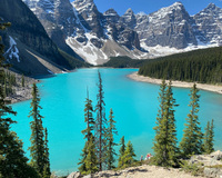 Turquoise Moraine Lake surrounded by snowy mountains and evergreen trees.