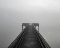 A wooden pier leading into dense fog with an overcast sky.