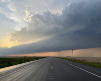 A straight road stretches into the distance beneath a dramatic sky with a sunset on the left and storm clouds on the right.