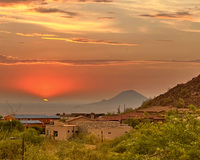 Desert sunset with vibrant orange sky over houses and a distant mountain.