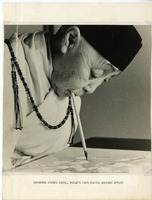 Elderly person painting with a brush held in their mouth, wearing traditional robes and a beaded necklace.

Text Section: "REVEREND JUNKO OISHI, WORLD'S MOST FAMOUS ARMLESS ARTIST"