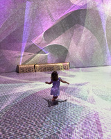 A child in a purple dress runs across a room filled with purple and white light projections.