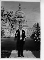 Man in tuxedo with Capitol building backdrop and flowering branches.