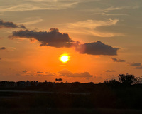 Sunset with an orange sky and scattered clouds above silhouetted trees and landscape.
