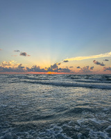 A sunrise over the ocean with gentle waves and scattered clouds.