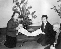 Three people kneeling on the floor examine a scroll with text.