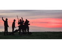 Silhouette of people with a cannon against a vivid sunset reflecting in water.