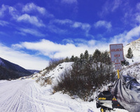 Snowy landscape with avalanche warning sign and partially covered snowmobile under a blue sky.