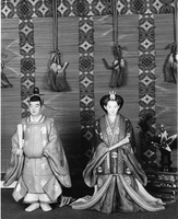 Two traditional Japanese dolls in front of a patterned backdrop with tassels.