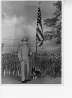 Statue of a military figure with a dog, an American flag, and a mural of soldiers in the background.
