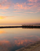 Sunset over a calm water body with vibrant reflections and a silhouetted pier.