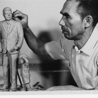 A man sculpting a statue of a man in a suit with a child beside it.