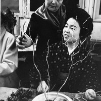 Two women arranging flowers, with branches and leaves on a table.