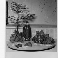 A model tree, a figurine in traditional attire, and rocks on a round base.