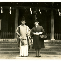 A man in traditional Japanese clothing and a woman in Western attire stand on steps outside a building. 