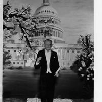 Man in tuxedo with Capitol building backdrop and flowering branches.