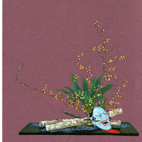 Still-life arrangement with a blue mask, budding branches, and textured objects on a dark platform.