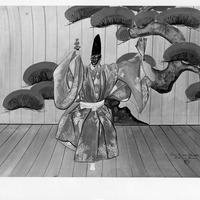 A person in traditional costume performing a dance with a fan, set against a backdrop of a stylized tree.