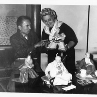 Two people examining traditional Japanese dolls on a table.