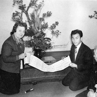Three people kneeling on the floor examine a scroll with text.