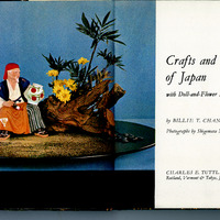 Cover of 'Crafts and Trades of Japan' featuring a doll dressed as a traditional Japanese tradesman seated beside a floral arrangement with yellow flowers and a wooden structure.