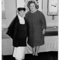 Two individuals in traditional and modern clothing stand in front of art-adorned walls.