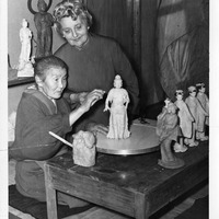 Two women sculpting figurines at a table with various clay statues.