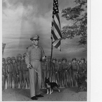 Statue of a military figure with a dog, an American flag, and a mural of soldiers in the background.